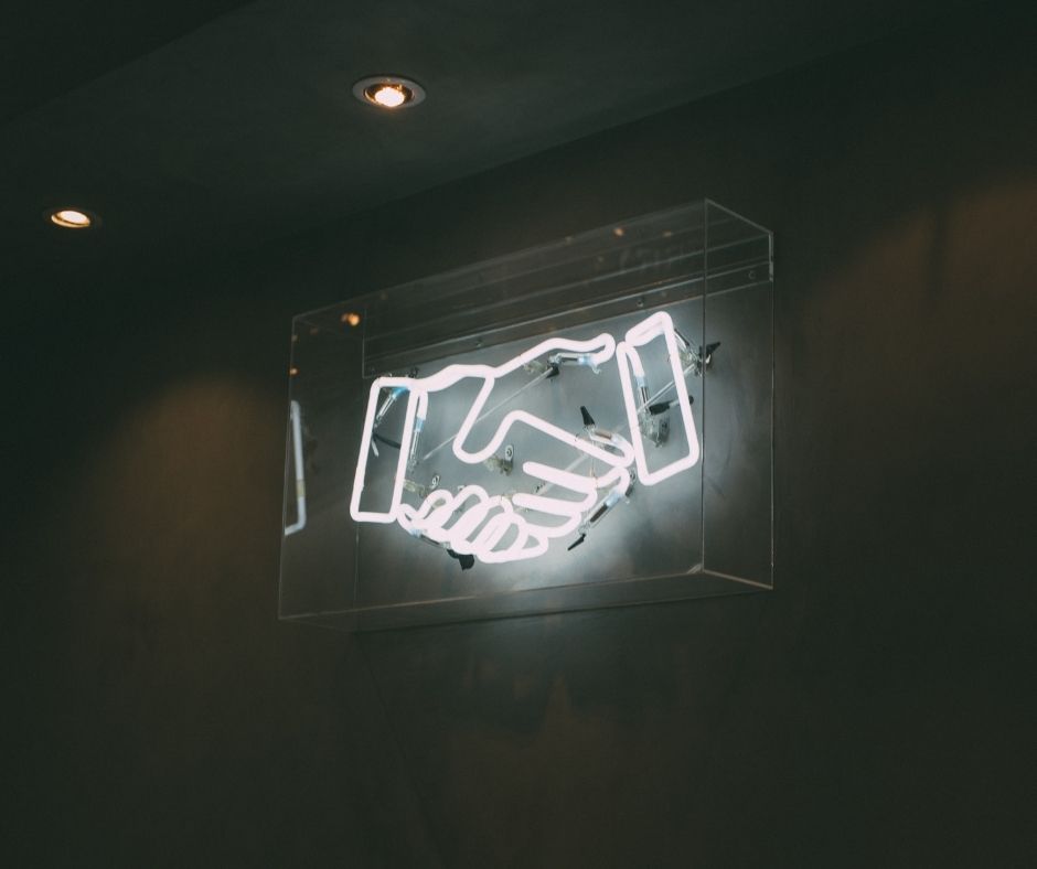 A photo of a neon sign with two hands shaking.